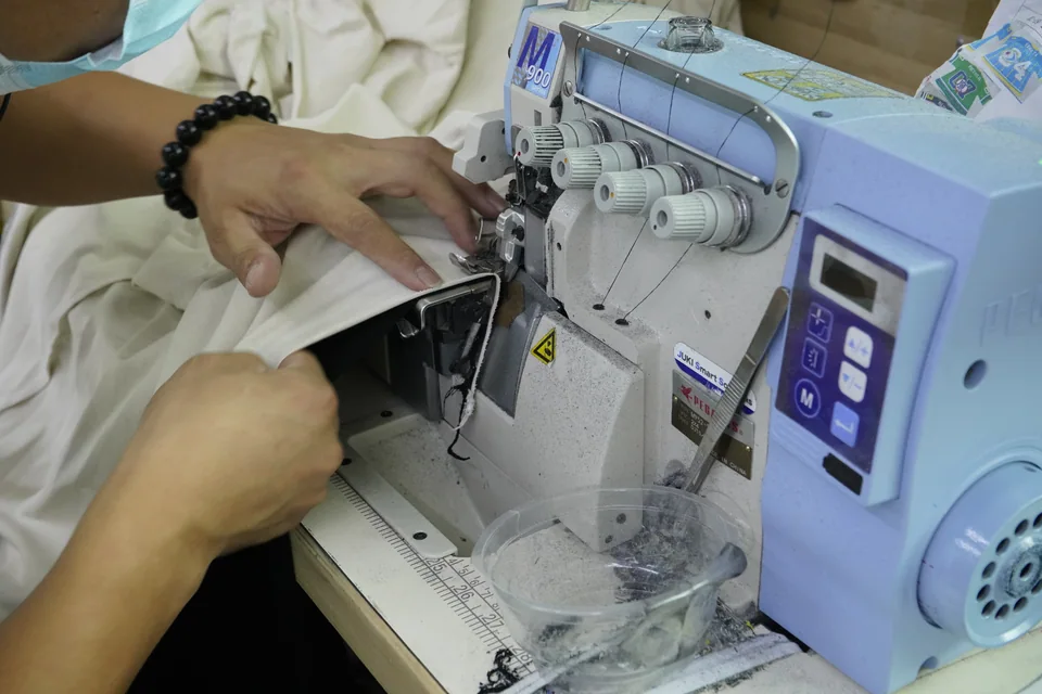 Hands guiding light-colored garment fabric through an industrial sewing machine