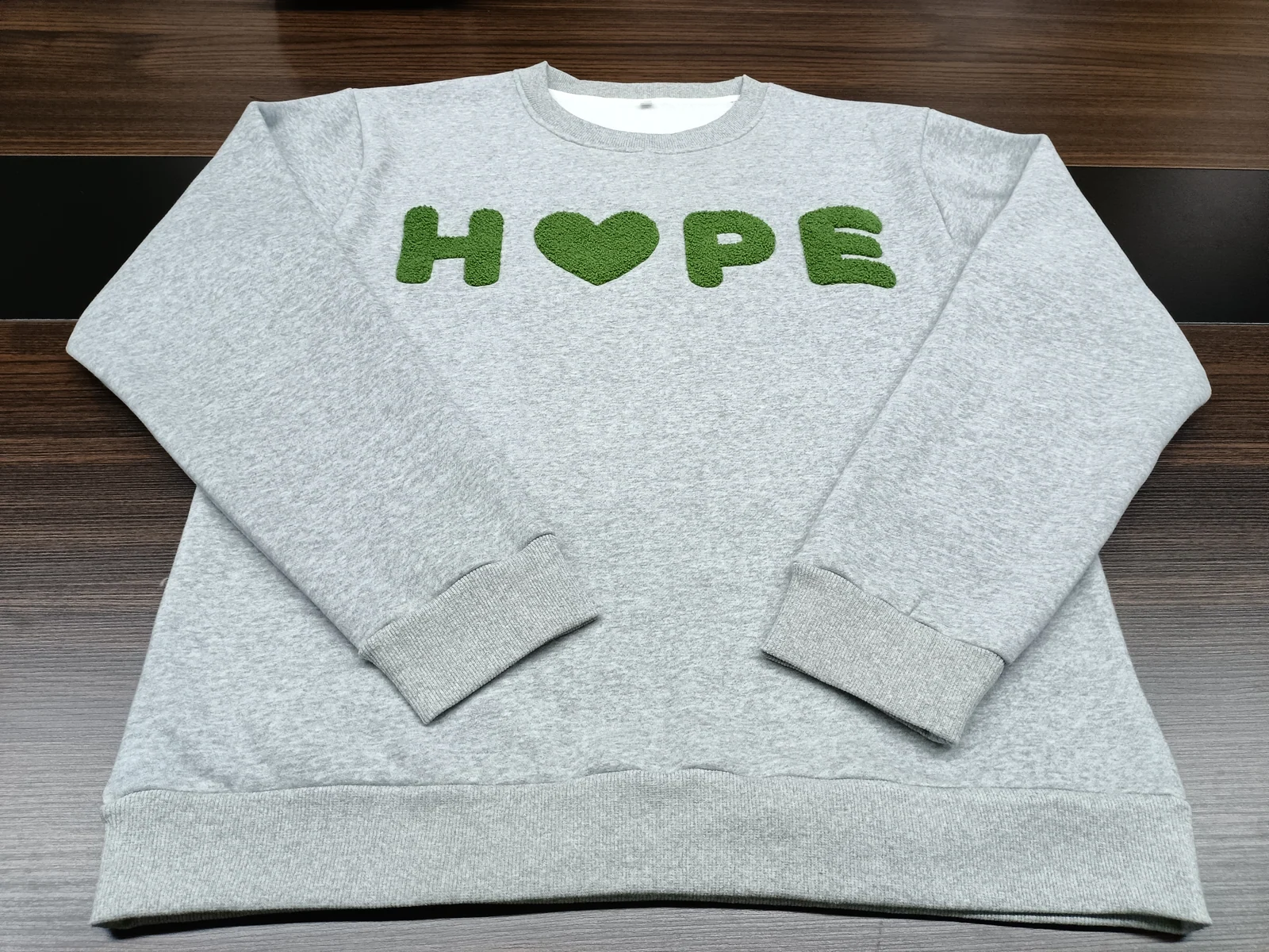 Gray crewneck sweatshirt with green raised lettering and a heart-shaped character