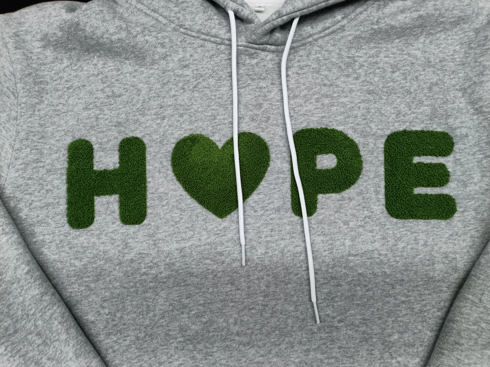 Close-up of green looped lettering and a heart shape on a gray hoodie
