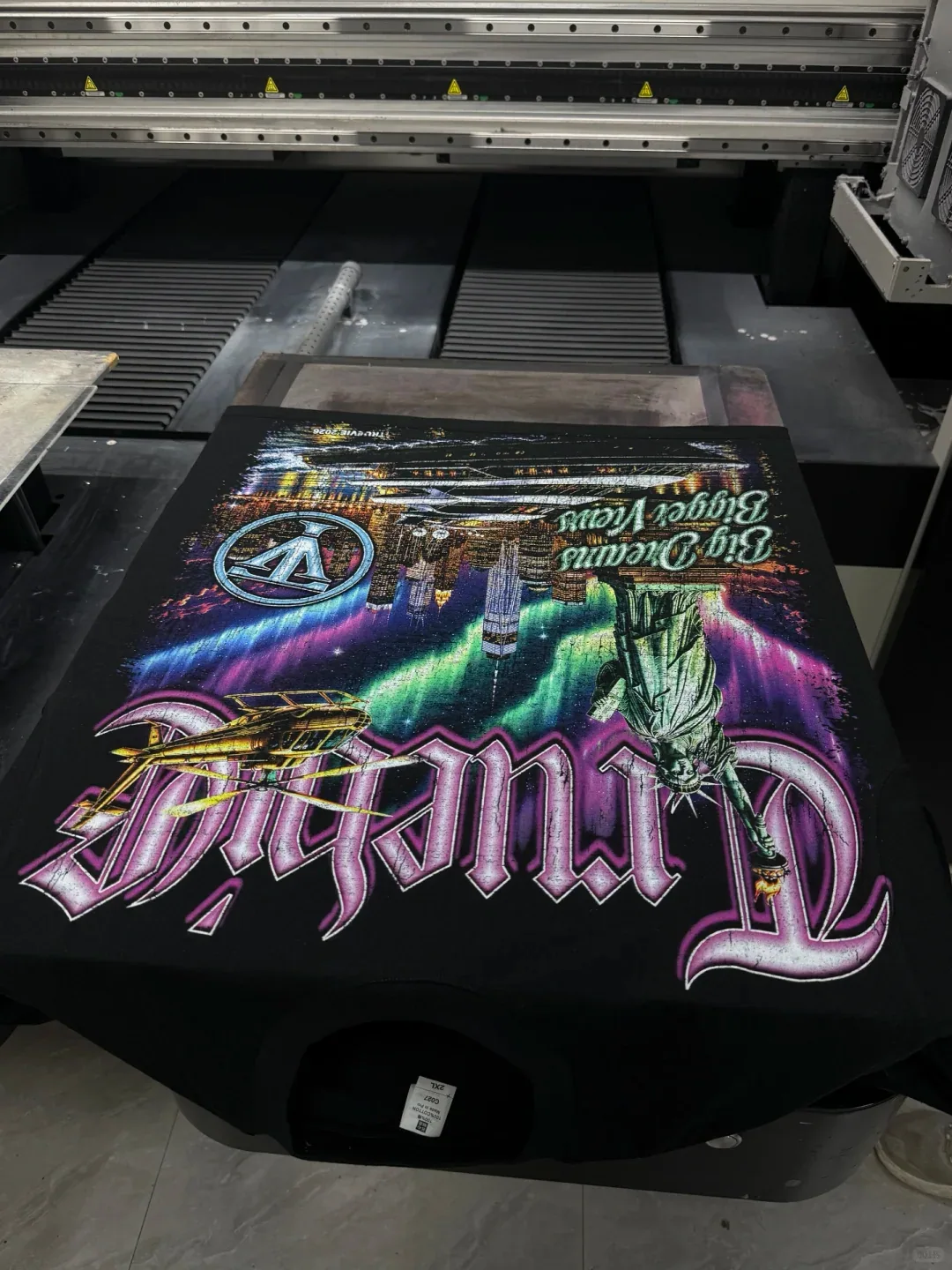 Dark T-shirt laid on a printer bed with a broad purple and green city-themed graphic