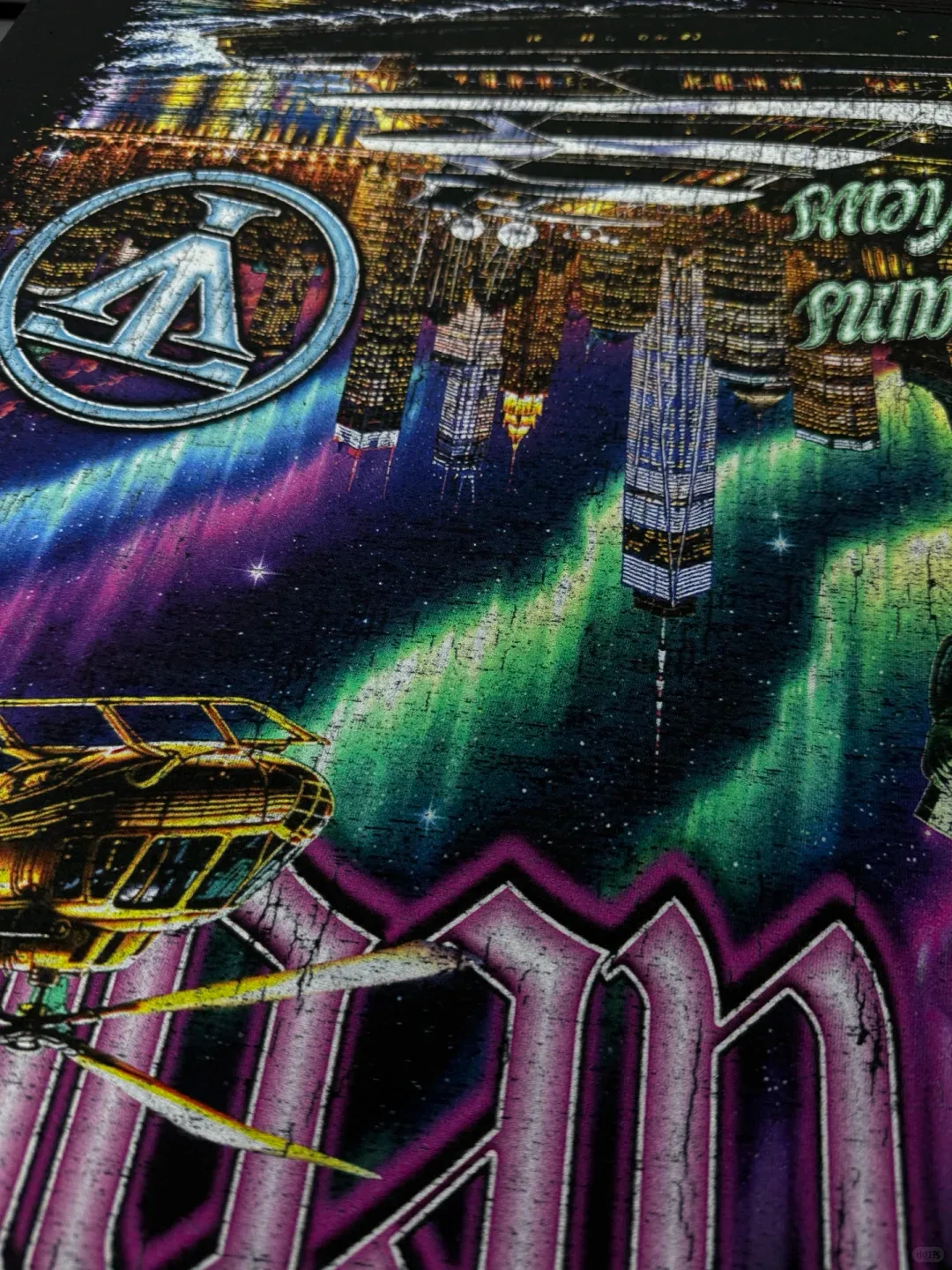 Detail of a purple and green large-format print with city buildings and outlined lettering on dark fabric