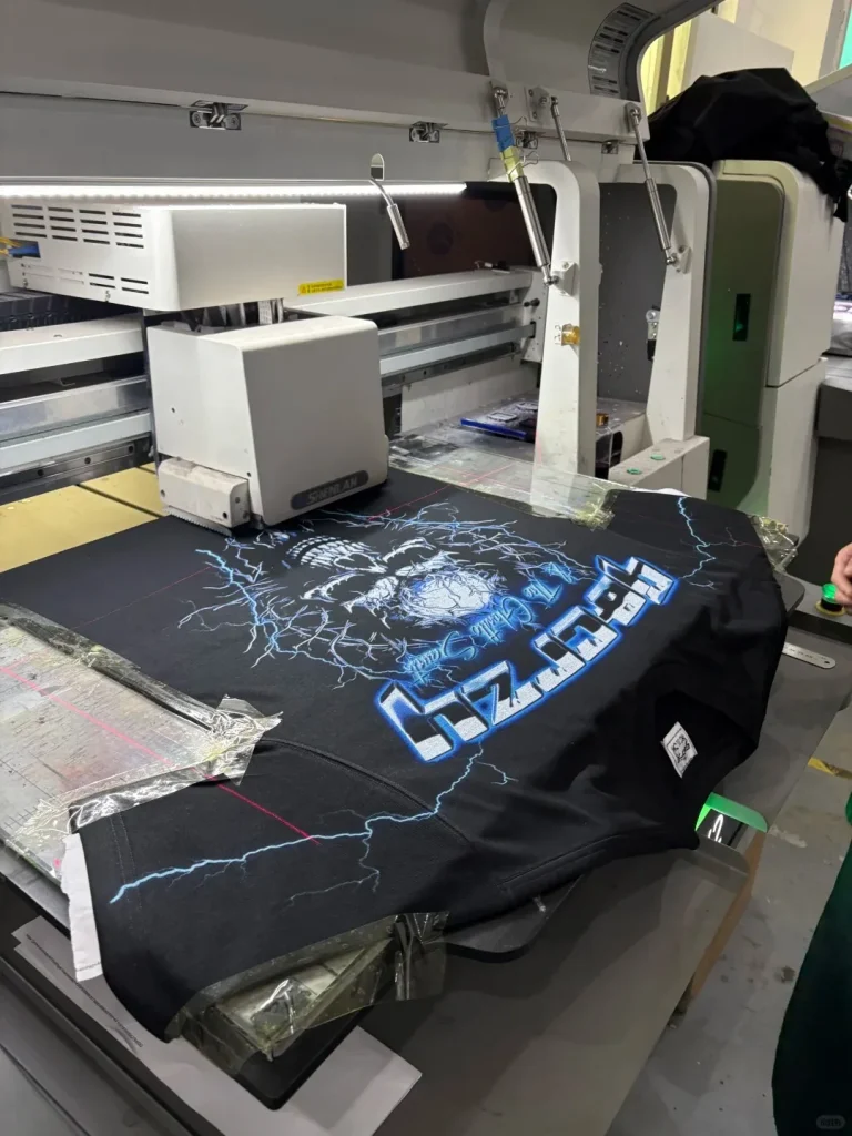 Garment printer working over a dark T-shirt with a large blue lightning and skull graphic