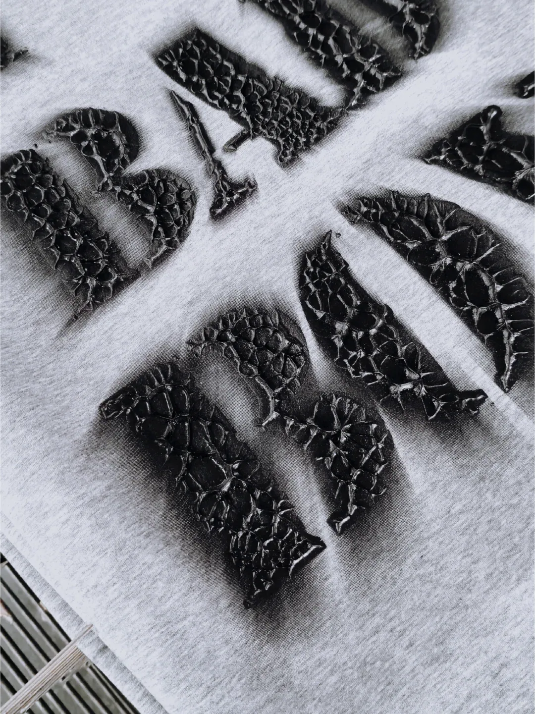 Angled view of black raised crackle-print letters on folded light gray fabric