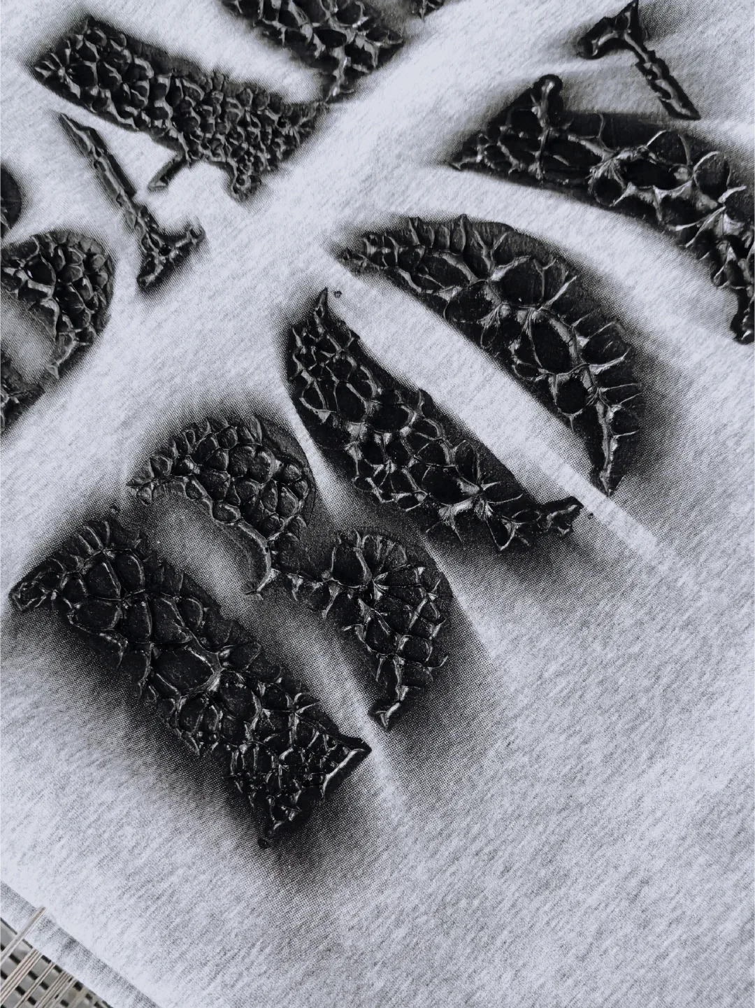 Black stone-effect lettering with a coarse cracked surface on light gray knit fabric