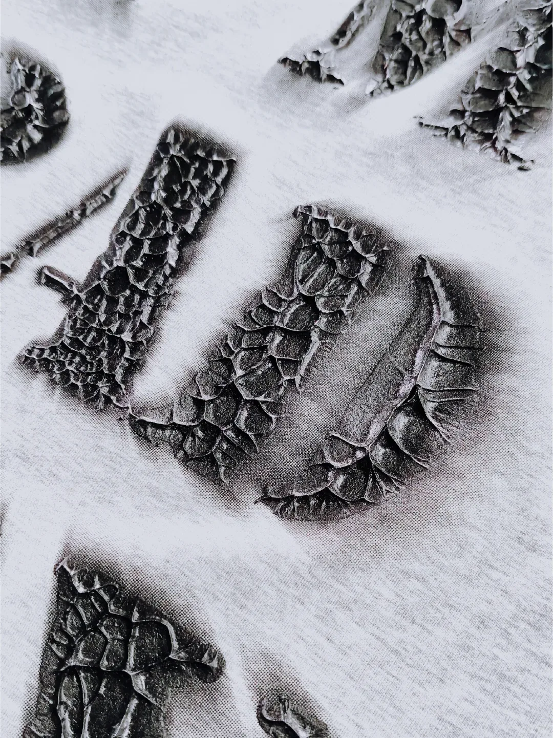 Raised black print with an uneven rock-like edge and deep surface fissures on gray fabric